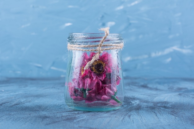 Bezpłatne zdjęcie szklany słoik ze sztucznymi fioletowymi kwiatami na niebiesko.