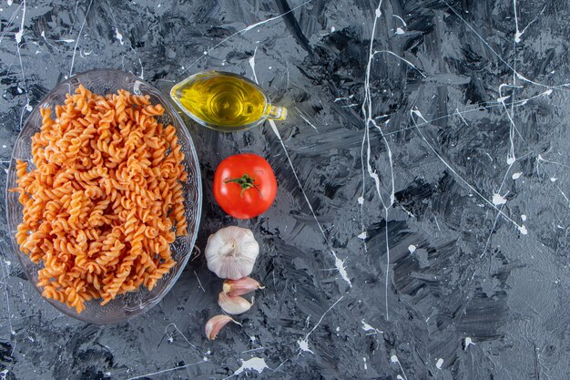 Szklany talerz pysznego makaronu fusilli i warzyw na tle marmuru.