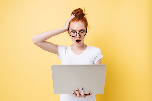 Szokująca imbirowa kobieta trzyma laptop i patrzeje w okularach