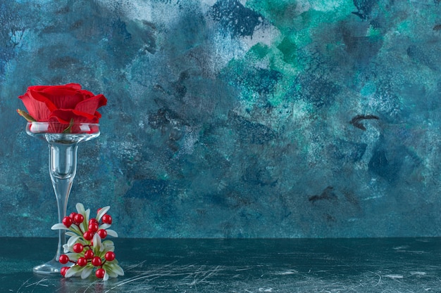 Sztuczna czerwona róża w szklanym cokole, na niebieskim tle.