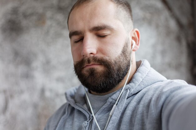 Sztuka ludzie emocje muzyka 4k i koncepcja stylu życia model wypuszczony mężczyzna w studio wkłada ucho telefony kołysze elektronikę do muzyki młody przystojny brodaty mężczyzna słucha muzyki smartfon w słuchawkach