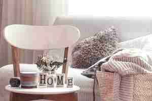Bezpłatne zdjęcie szykowne wnętrze domu. świece, wazon z kwiatami z drewnianymi literami domu na drewnianym białym krześle. sofa i wiklinowy kosz z poduszkami w tle. dekoracja domowa.