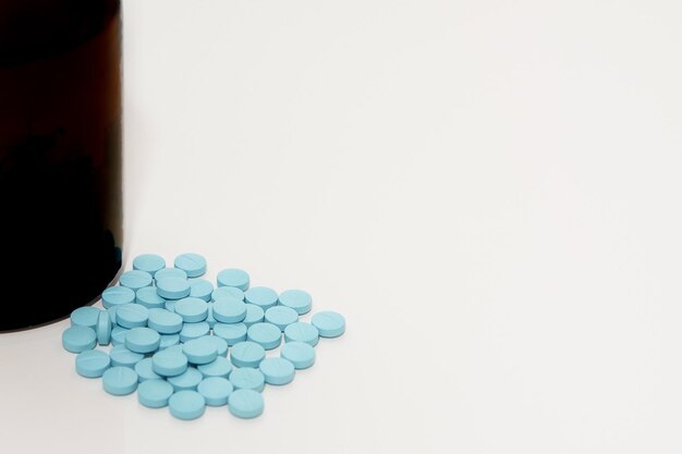 Tabletki medyczne blue pills na podłodze obok butelki na białym z miejscem na kopię
