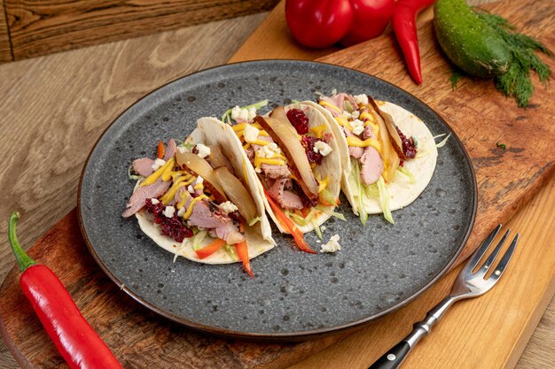 Tacos z wędzonym mięsem podawane na czarnym talerzu.