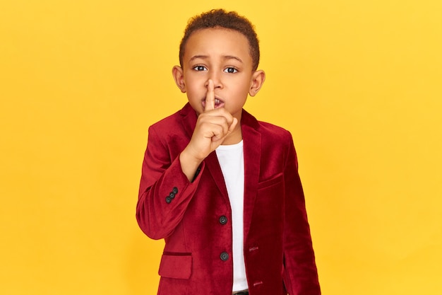 Tajemniczy chłopak w stylowych ubraniach robi gest uciszenia z palcem wskazującym na ustach