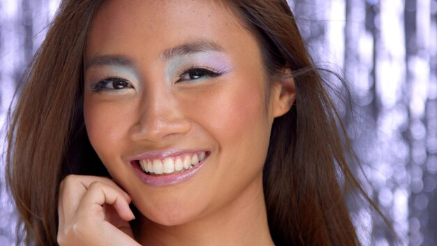 Tajski model azjatycki w studio ze srebrnym deszczowym tłem disco i uśmiechniętym makijażem imprezowym
