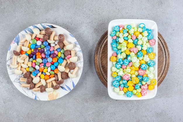 Bezpłatne zdjęcie talerz cukierków i pieczarek czekoladowych obok talerza cukierków popcornowych na drewnianej tacy na marmurowej powierzchni