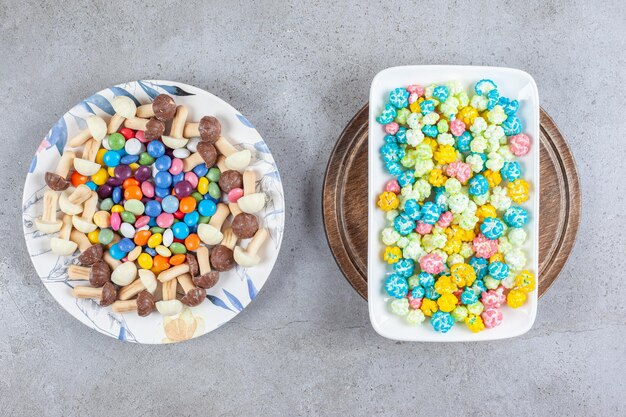 Talerz cukierków i pieczarek czekoladowych obok talerza cukierków popcornowych na drewnianej tacy na marmurowej powierzchni