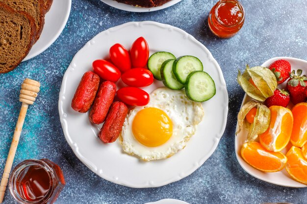 Talerz śniadaniowy zawierający kiełbaski koktajlowe, jajka sadzone, pomidorki koktajlowe, słodycze, owoce i szklankę soku brzoskwiniowego.