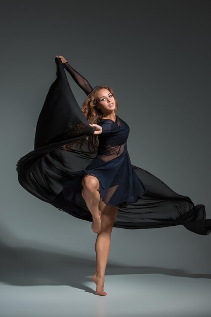 Tańcząca kobieta w czarnej sukience. Współczesny taniec nowoczesny na szarym tle. Fitness, model rozciągający