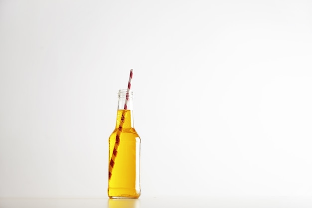 Bezpłatne zdjęcie tastu musujący żółty napój ze słomką w czerwone paski wewnątrz otwartej rustykalnej szklanej butelki na białym tle