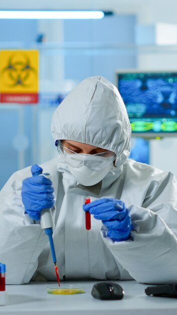 Technik naukowy w kombinezonie ppe przy użyciu mikropipety i szalki Petriego pracujący w laboratorium badawczym analizującym próbkę krwi. Zespół badający ewolucję wirusa w celu opracowania szczepionki przeciwko Covid19