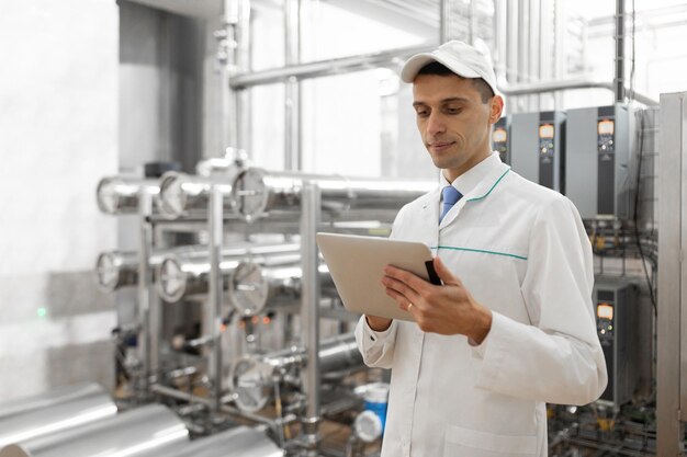 Technolog w białym fartuchu z tabletem w rękach kontroluje proces produkcji w mleczarni Kontrola jakości w mleczarni