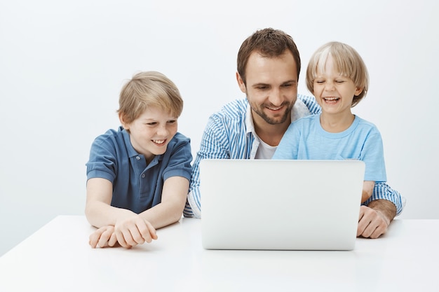 Technologia jednoczy rodzinę. Portret szczęśliwy, piękny ojciec i synowie siedzący w pobliżu laptopa i uśmiechając się szeroko, dobrze się bawią