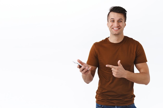 Technologia online styl życia i koncepcja komunikacji Szczęśliwy kaukaski mężczyzna prezentuje aplikację na smartfona wskazując na komórkę z zadowolonym promiennym uśmiechem opisz nową aplikację zakupy w Internecie