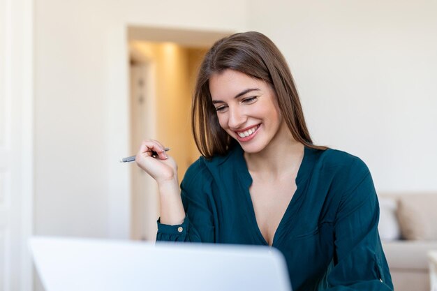 Technologia pracy zdalnej i koncepcja ludzi szczęśliwa uśmiechnięta młoda kobieta biznesu z laptopem i papierami pracującymi w domowym biurze