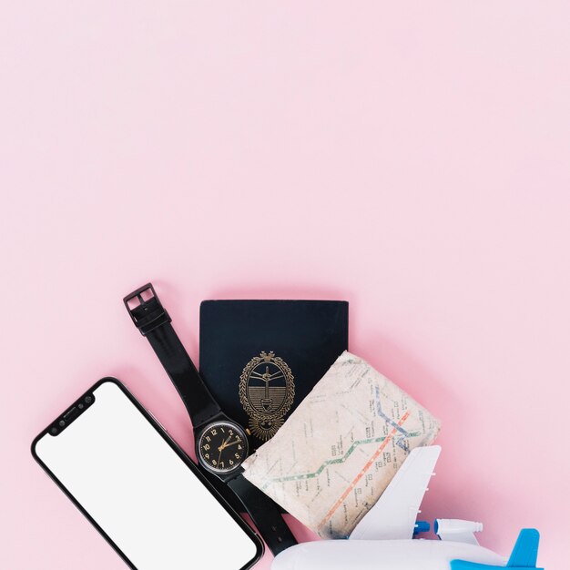 Telefon komórkowy; zegarek na rękę; paszport; mapa i miniaturowy samolot na różowym tle