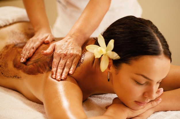Terapeuta zbliżenie masujący plecy kobiety podczas zabiegu gorącej czekolady w spa