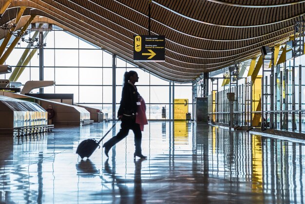 Terminal lotniska z ludźmi poruszającymi się sylwetkami i promieniami słońca