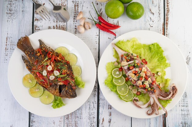 Tilapia smażona z sosem chili i kałamarnicą, cytryną i czosnkiem na talerzu na białym drewnianym stole.