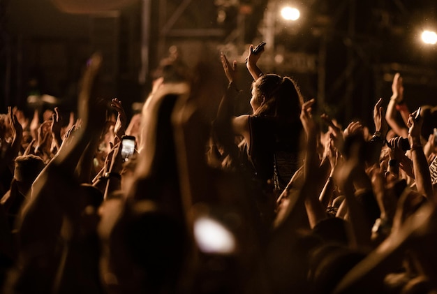 Tłum ludzi z podniesionymi rękami bawiącymi się nocą na festiwalu muzycznym
