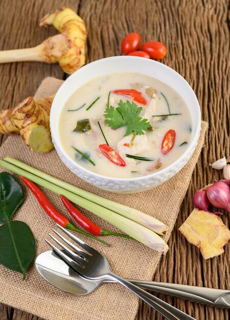 Tom Kha Kai w misce z liśćmi limonki kaffir, trawą cytrynową, czerwoną cebulą, galangą i chili.