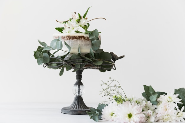 Tort weselny na cakestand ozdobiony bukietem białych kwiatów