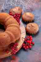 Bezpłatne zdjęcie tortowe babeczki z widokiem z boku obok deski do krojenia z ciastem i czerwonymi porzeczkami