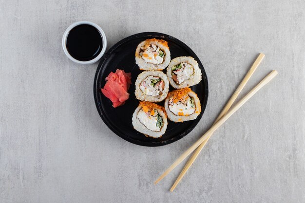 Tradycyjne roladki sushi ozdobione chrupiącymi frytkami na czarnym talerzu.