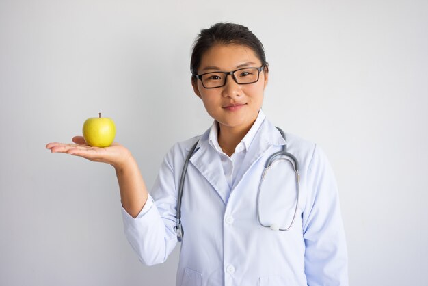 Treści młoda Azjatycka kobiety lekarki mienia jabłko na palmie.