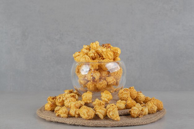 Trivet spoczywa pod pełną szklaną misą otoczoną popcornem pokrytym karmelem na marmurowym stole.