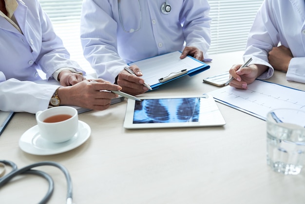 Bezpłatne zdjęcie trzech przyciętych lekarzy analizujących prześwietlenie klatki piersiowej na cyfrowej podkładce