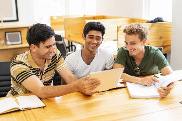 Trzech studentów roześmiany studia, przeglądanie na tablecie