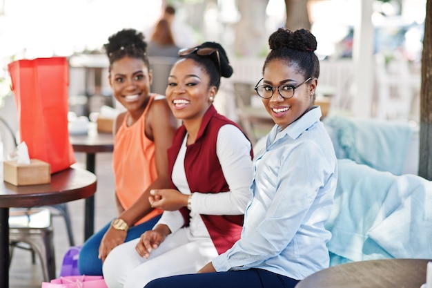 Trzy afroamerykańskie dziewczyny na co dzień z kolorowymi torbami na zakupy chodzą na świeżym powietrzu Stylowe zakupy dla czarnych kobiet