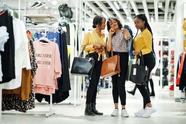 Trzy Afrykanki w sklepie odzieżowym z nowymi torebkami Dzień zakupów Patrzą na telefony komórkowe