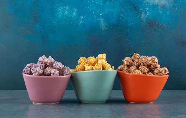 Trzy kolorowe miseczki wypełnione różnymi smakami popcornu na niebieskim tle. zdjęcie wysokiej jakości