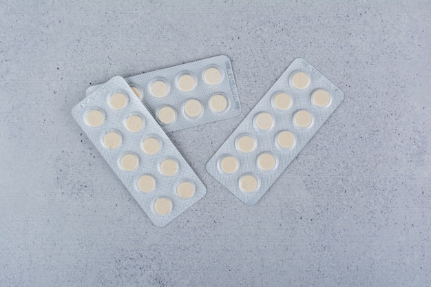 Trzy opakowania okrągłych tabletek leku na tle marmuru.