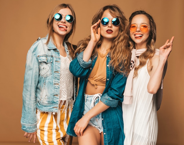 Trzy piękne uśmiechnięte dziewczyny w modne letnie ubrania i okulary przeciwsłoneczne. Seksowny beztroski kobiet pozować. Pozytywne modele. Pokazuje język