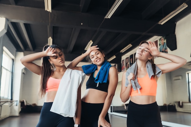 Trzy szczęśliwe uśmiechnięte pozytywne dziewczyny po treningu na siłowni. Patrzą w kamerę. Poziomy.