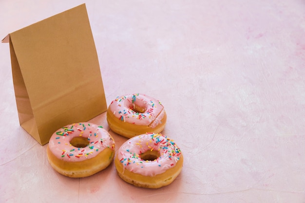 Bezpłatne zdjęcie trzy wyśmienicie donuts z pakuneczkiem na różowym tle