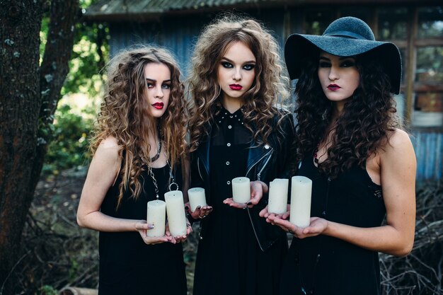 Trzy zabytkowe kobiety jako czarownice, pozy i trzymające w dłoniach świece w przeddzień Halloween