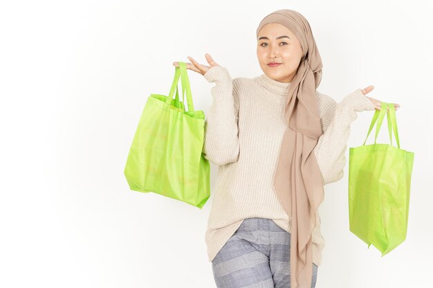 Trzymając zieloną torbę na zakupy pięknej azjatyckiej kobiety noszącej hidżab na białym tle