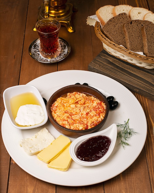 Tureckie śniadanie menemen z miodem, śmietaną, oliwkami, dżemem i odmianami sera w białym talerzu i szklance herbaty