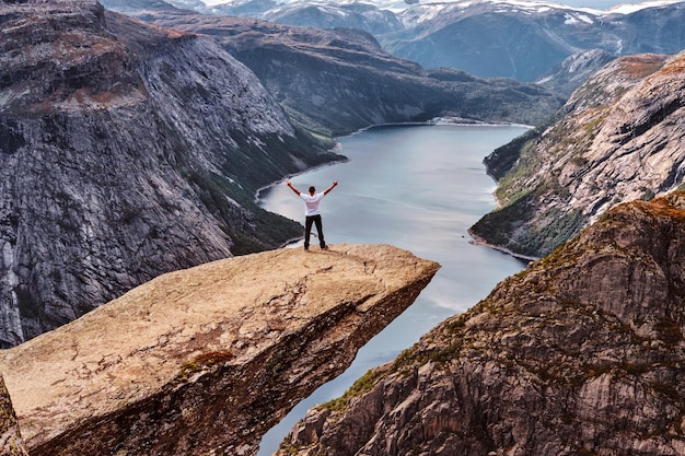 Bezpłatne zdjęcie turysta mężczyzna stojący w trolltunga i cieszy się pięknym widokiem na norweski fiord.