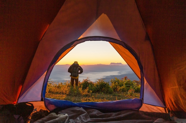 Turysta stoi na kempingu w pobliżu pomarańczowego namiotu i plecaka w górach