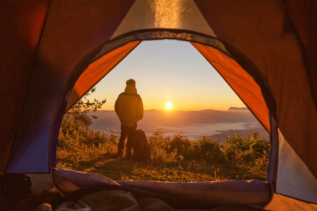 Turysta stoi na kempingu w pobliżu pomarańczowego namiotu i plecaka w górach