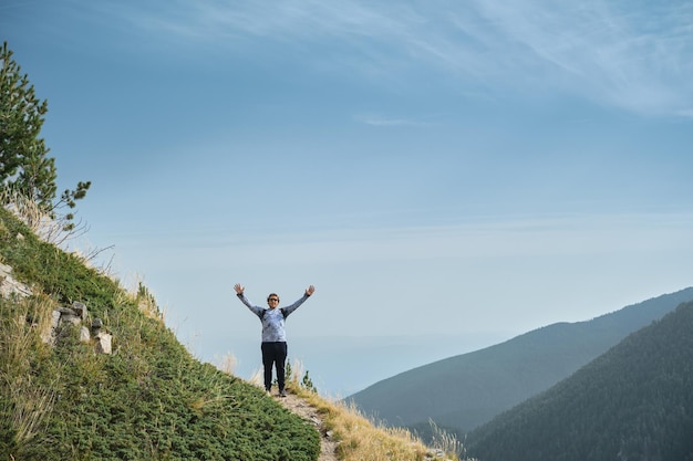 Bezpłatne zdjęcie turysta z podniesionymi rękami stoi na przełęczy, wspinając się po górach i ciesząc się triumfem