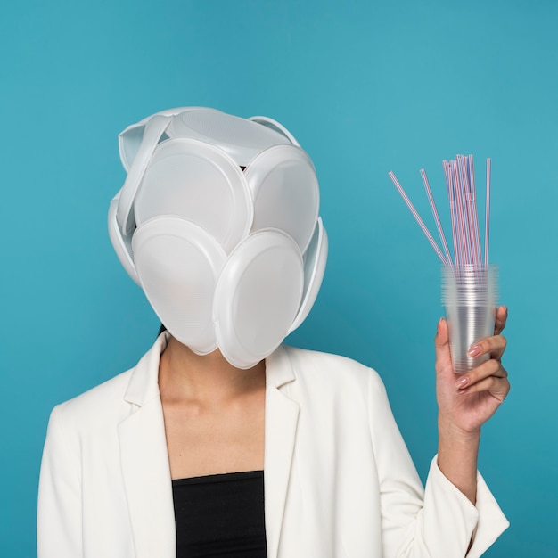 Bezpłatne zdjęcie twarz kobiety pokryta plastikowymi talerzami i trzymająca plastikowe kubki i słomki
