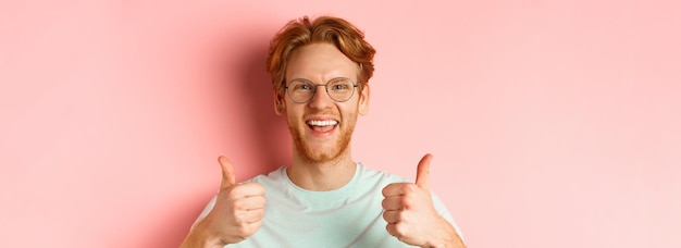 Bezpłatne zdjęcie twarz zadowolonego męskiego klienta pokazującego kciuk w aprobacie, uśmiechniętego szczęśliwego w okularach i tshir