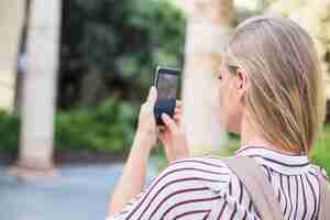 Bezpłatne zdjęcie tylni widok bierze fotografię na telefonie komórkowym blondynki młoda kobieta